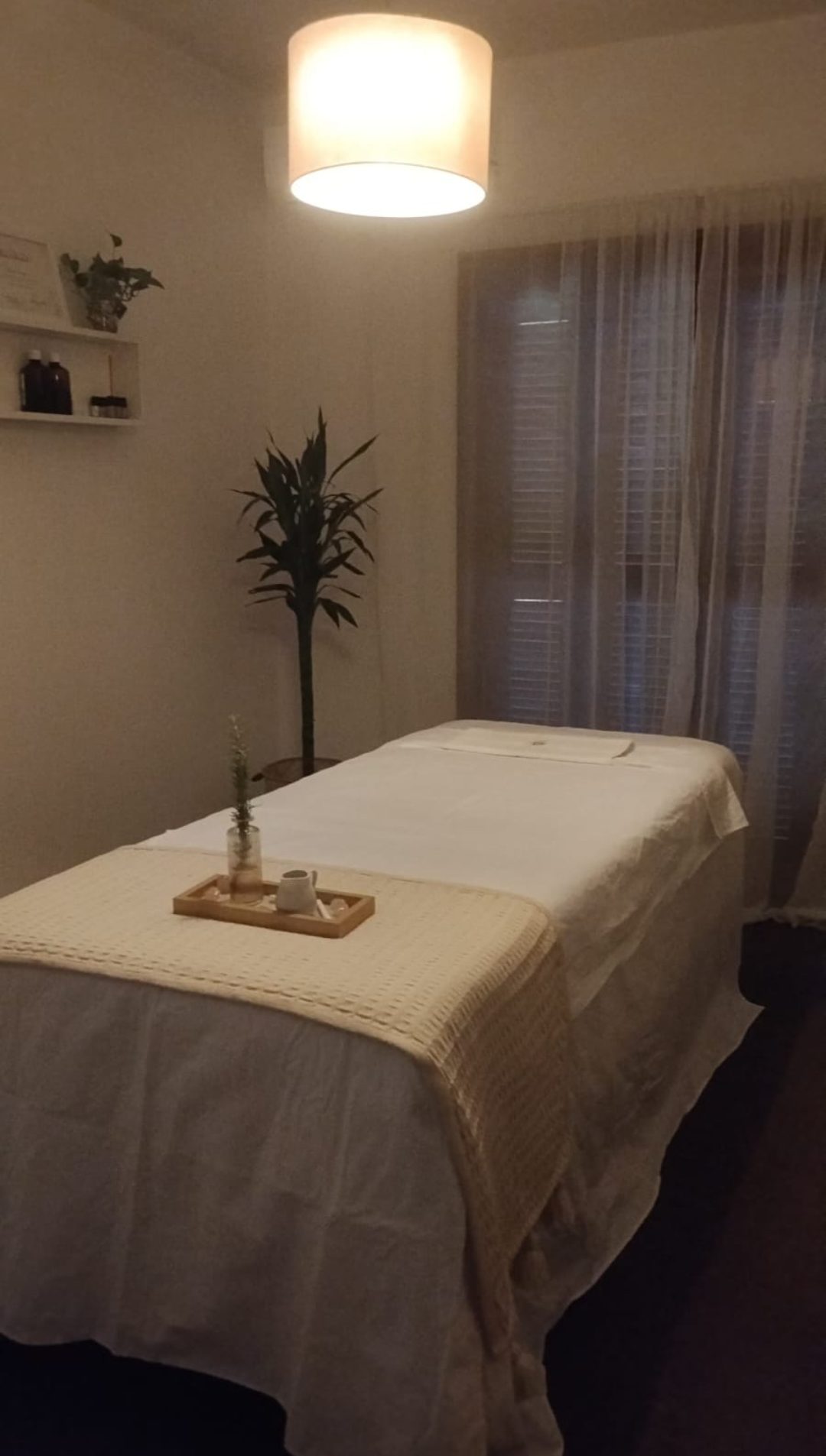 Sala de massagem: maca com lençóis claros, luz suave e plantas.